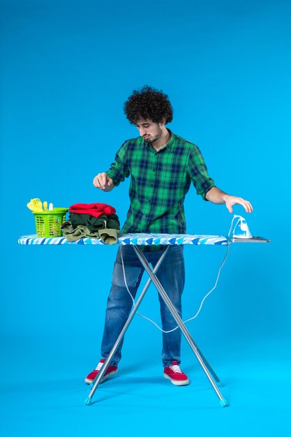 vista frontale giovane maschio con asse da stiro su sfondo blu colore casa lavatrice lavori domestici pulizia umana