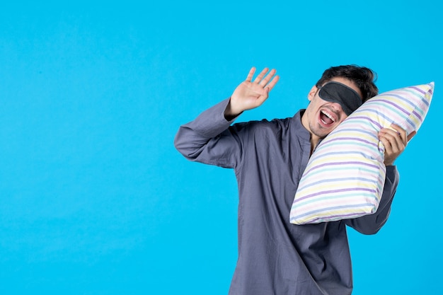 vista frontale giovane maschio in pigiama che cerca di addormentarsi sul cuscino su sfondo blu sveglia umana riposo a letto notte a colori sonno in ritardo