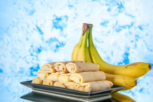 Vista frontale gustose frittelle arrotolate con banane su sfondo azzurro mattina colore latte colazione dessert dolce torta zucchero