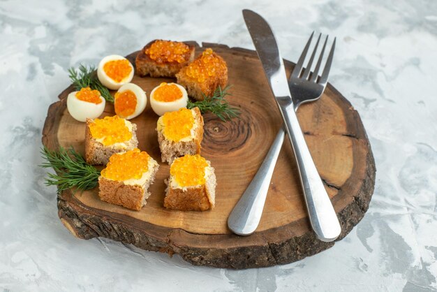Vista frontale gustosi panini al caviale con uova sode e posate su tavola di legno sfondo bianco cibo colazione pranzo frutti di mare pesce toast