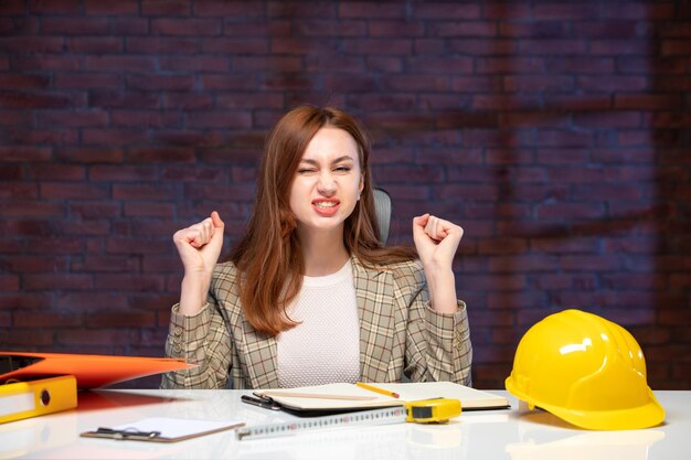 vista frontale ingegnere donna seduta dietro il suo posto di lavoro in cantiere agenda lavoro costruttore appaltatore successo aziendale piano proprietà