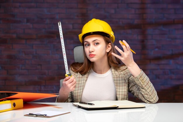 vista frontale ingegnere donna seduta dietro il suo posto di lavoro tenendo il metro a nastro agenda lavoro proprietà aziendale business plan successo builder