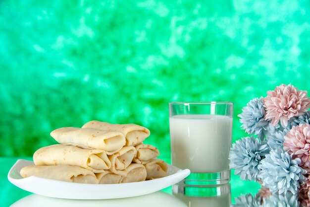 Vista frontale laminati frittelle dolci con un bicchiere di latte su sfondo verde pasto torta colazione cibo colore mattina fiore di zucchero