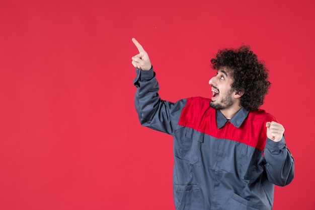 Vista frontale lavoratore maschio in uniforme che punta sopra su sfondo rosso uniforme lavoro colore strumento casa foto strumento lavoratore meccanico