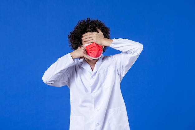 Vista frontale medico maschio in tuta medica e maschera che imita la telefonata su sfondo blu vaccino farmaco ospedale virus covid- salute pandemica