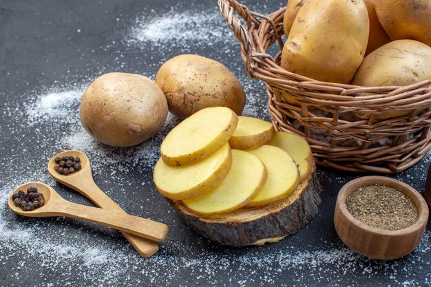 Vista frontale ravvicinata di patate fresche intere e tritate su spezie di tavola di legno su sfondo di colori misti bianco nero