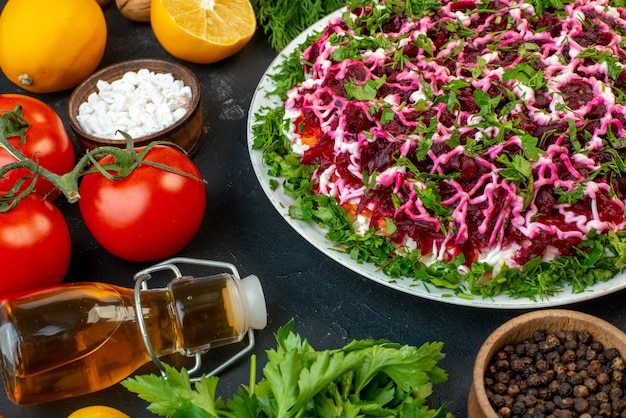 Vista frontale ravvicinata di una deliziosa insalata decorata con verdure fresche verdi e zenzero giallo bottiglia di olio caduta su sfondo nero