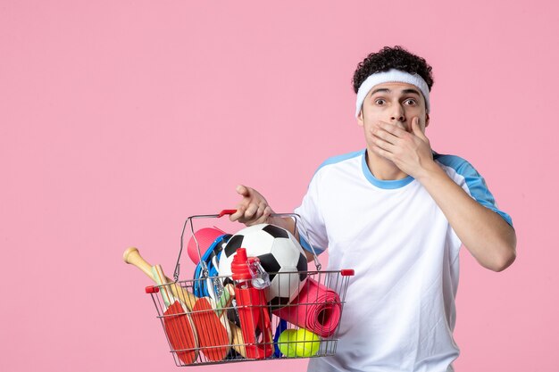 Vista frontale scioccato giovane maschio in abiti sportivi con cesto pieno di cose sportive