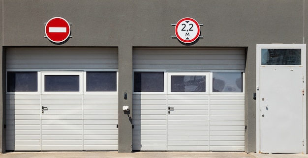 Vista frontale su due cancelli bianchi chiusi del garage e porta d'ingresso, pareti modanature grigie e segnali stradali su di esso