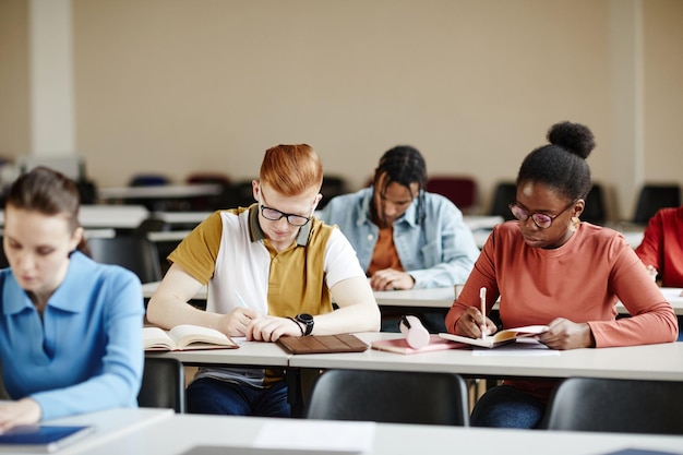 Vista frontale su un gruppo eterogeneo di studenti che prendono appunti durante le lezioni nello spazio della copia del college o dell'università