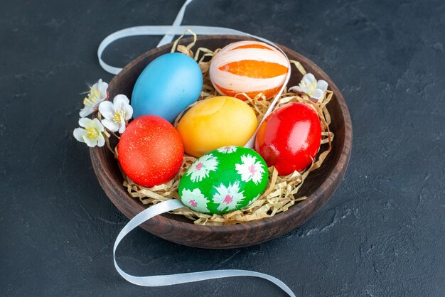 vista frontale uova di pasqua colorate all'interno del piatto con paglia su superficie scura concetto di vacanza primaverile ornato multi gruppo