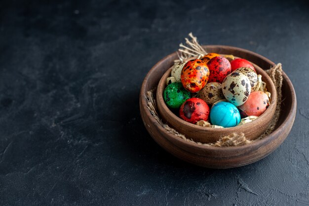 vista frontale uova di pasqua colorate all'interno del piatto marrone su superficie scura dark