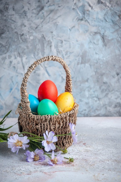 vista frontale uova di pasqua colorate all'interno di un bellissimo cesto su superficie bianca