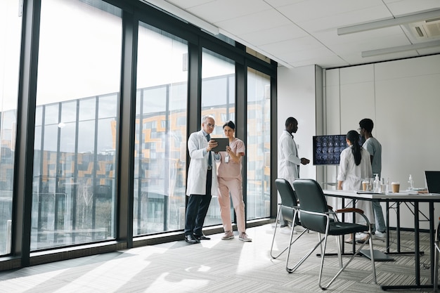 Vista grandangolare a diversi gruppi di medici nella sala conferenze che discutono di lavoro, copia spazio