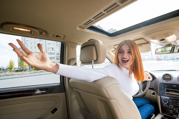 Vista grandangolare del giovane autista della donna di redhead che conduce un'automobile indietro guardando.