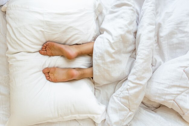 Vista in primo piano dei piedi sdraiati sul morbido cuscino bianco a letto