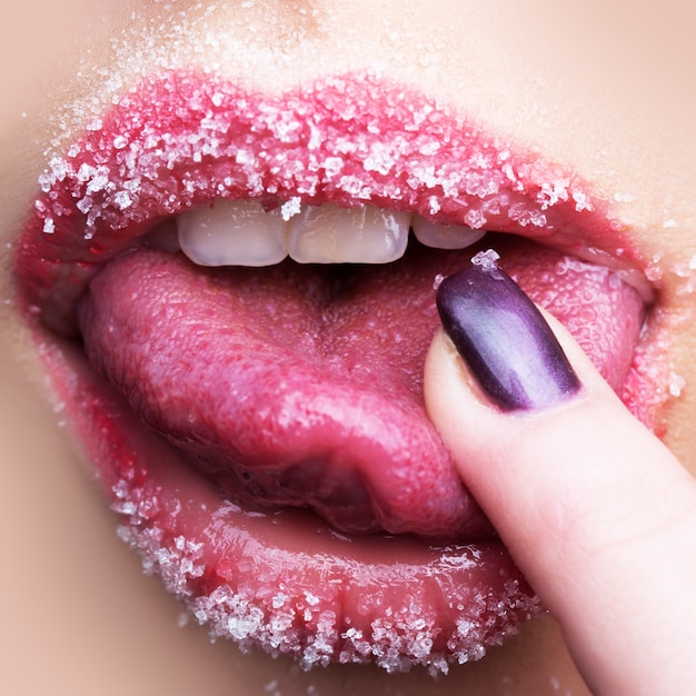 Vista in primo piano della parte del corpo facciale di belle labbra femminili aperte sessuali con rossetto a velo di zucchero e denti bianchi che toccano la lingua con il dito, immagine quadrata square