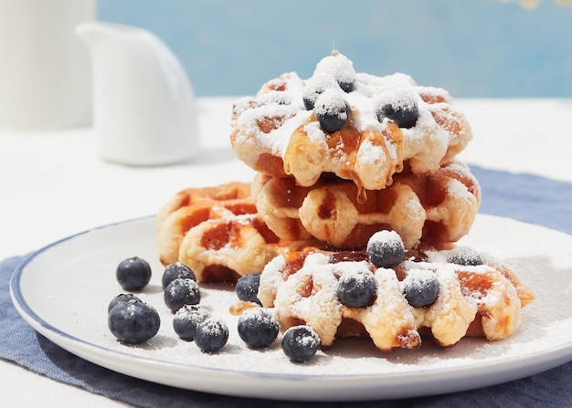 Vista ingrandita dei waffle belgi con mirtilli zucchero a velo in cima con sciroppo gocciolante