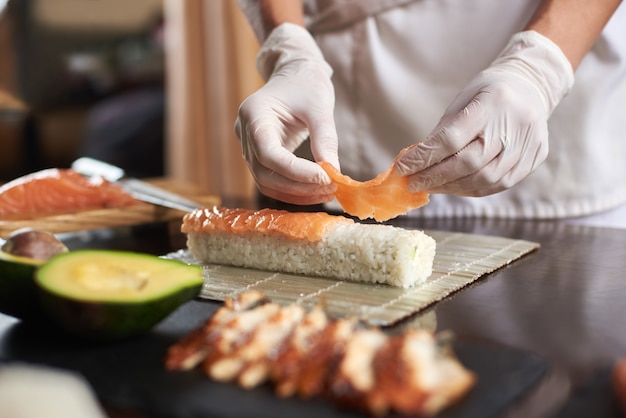 Vista ingrandita del processo di preparazione del sushi di laminazione con guanti monouso sulla stuoia di bambù