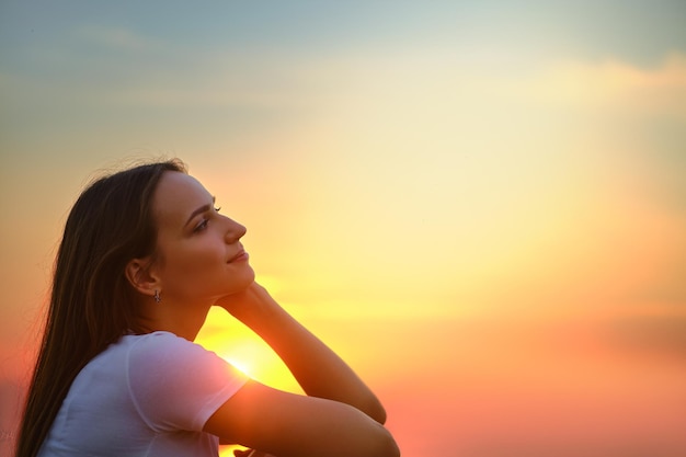 Vista ingrandita della giovane donna seduta su un molo e guardare il tramonto