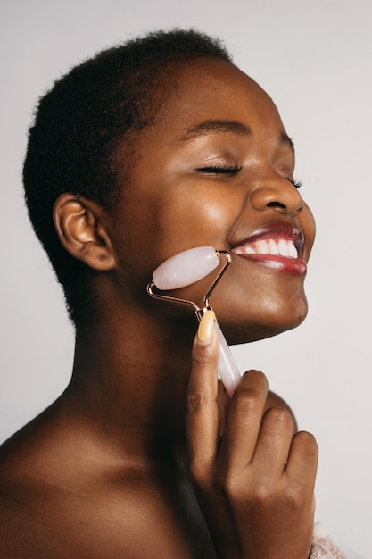 Vista ingrandita di una donna afroamericana che usa il rullo facciale in pietra di giada e il sorriso con gli occhi chiusi i