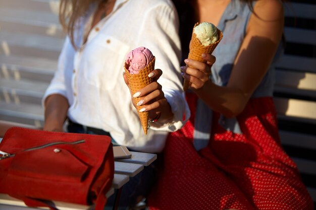 Vista isolata di due amiche sedute e in possesso di due coni gelato nelle loro mani