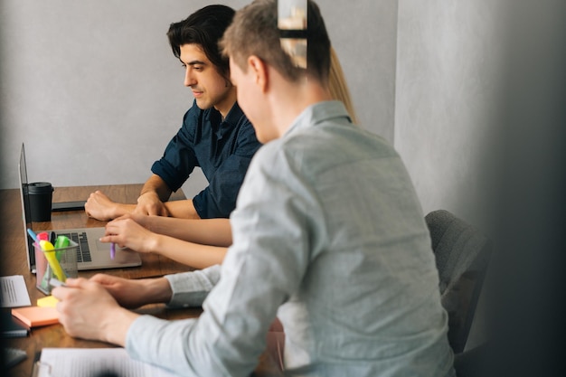 Vista laterale dei dipendenti di sesso maschile e femminile seduti alla scrivania dell'ufficio che guardano lo schermo del laptop che collaborano in ufficio Colleghi concentrati fanno brainstorming insieme nella sala riunioni Concetto di riunione di lavoro aziendale