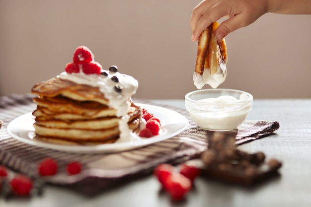 Vista laterale dei pancake tradizionali della famiglia con panna acida e bacche fresche isolate su oscurità