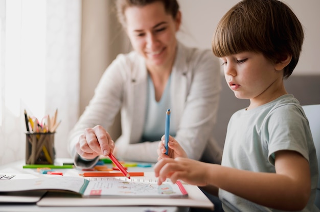 Vista laterale del bambino che studia a casa con l'aiuto del tutor