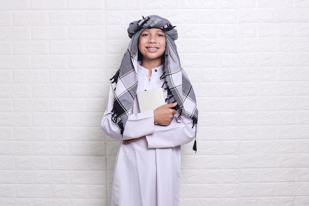 Vista laterale del bambino musulmano che indossa stile arabo e turbante che tiene il corano