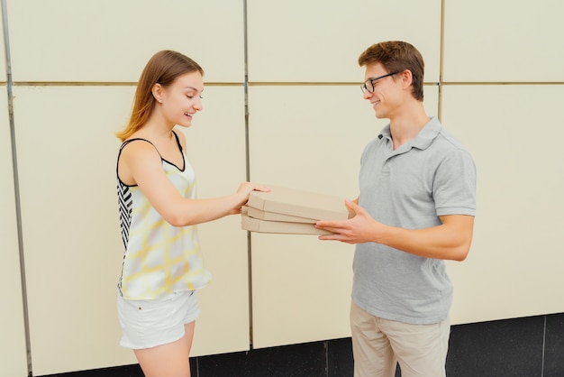 Vista laterale del bel ragazzo dando una pizza alla ragazza attraente, mentre lei sta controllando la pizza nella scatola, all'aperto. Vestito con abiti alla moda estivi.