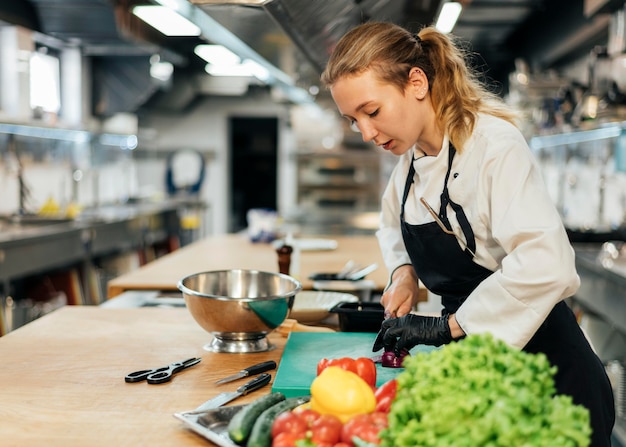 Vista laterale del cuoco unico femminile che prepara insalata con le verdure