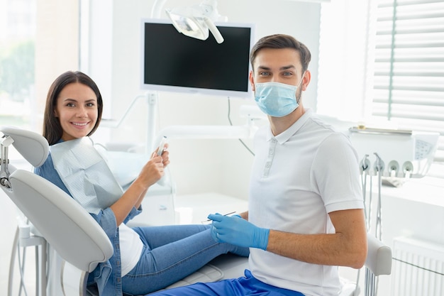 Vista laterale del dentista maschio in maschera con parient seduto sulla poltrona del dentista guardando la telecamera