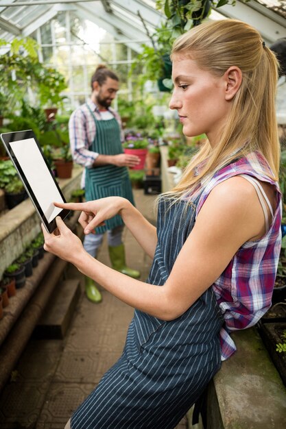 Vista laterale del giardiniere femminile che per mezzo della compressa digitale alla serra