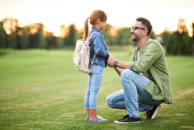 Vista laterale del gioioso giovane padre che sorride mentre tiene le mani delle figlie papà che trascorre del tempo con il suo