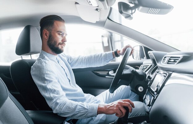 Vista laterale del giovane bell'uomo in abiti formali seduto in un'automobile nuova di zecca