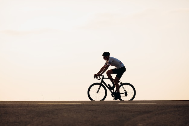 Vista laterale del giovane ciclista in abbigliamento sportivo e casco protettivo in sella alla bici all'aperto
