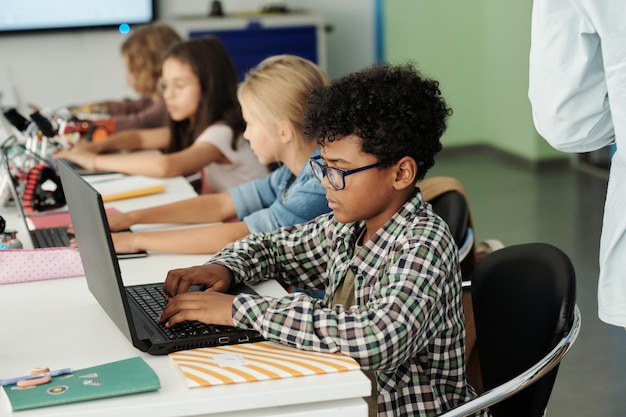 Vista laterale del giovane scolaro afroamericano che lavora davanti al computer portatile