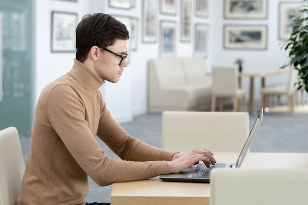Vista laterale del giovane sviluppatore di società di tecnologia che digita sulla tastiera del laptop
