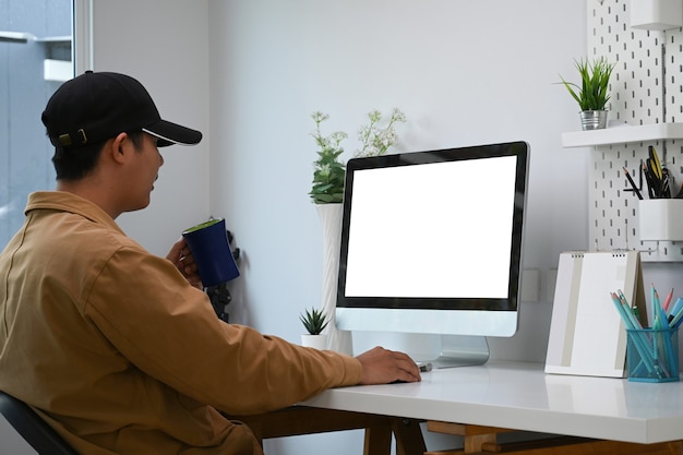 Vista laterale del giovane uomo asiatico che lavora in linea sul computer moderno nel suo ufficio a casa