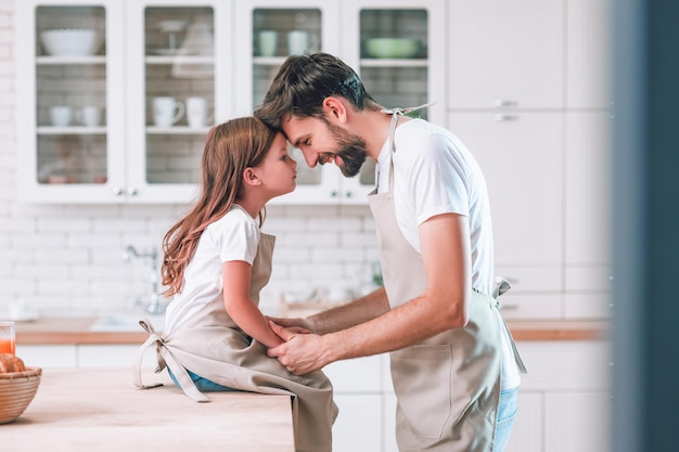 Vista laterale del padre e della ragazza che indossano grembiuli che si guardano in cucina