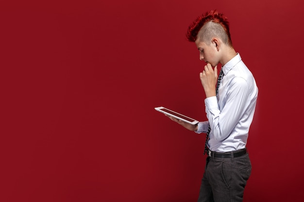 Vista laterale del punk teenager dai capelli rossi con la compressa contro lo spazio rosso isolato