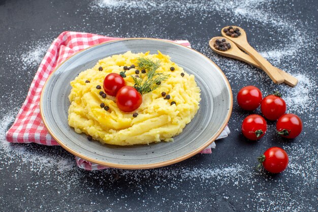 Vista laterale del purè di patate servito con pomodori pepe aneto su asciugamano rosso spogliato su sfondo bianco nero misto colore