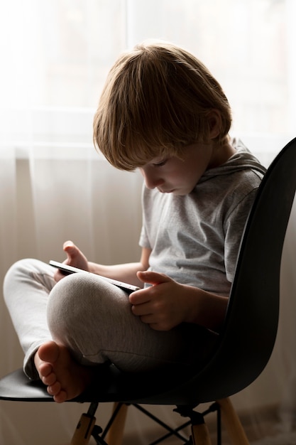 Vista laterale del ragazzo seduto in salmerino e utilizzando tablet