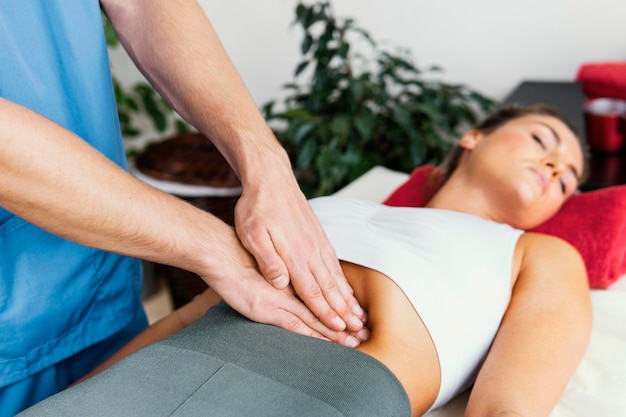 Vista laterale del terapista osteopatico maschio che controlla l'addome della donna