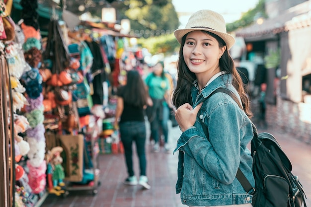 vista laterale del viaggiatore con zaino e sacco a pelo femminile asiatico attraente a los angeles usa durante la pausa estiva. giovane ragazza turista viso fotocamera sorridente adorabile in piedi su Olvera Street. donna viaggiatore mercato locale del Messico