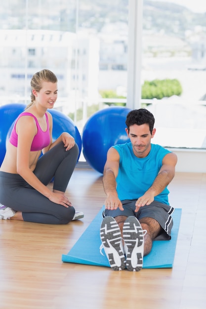 Vista laterale dell&#39;addestratore femminile che aiuta uomo con i suoi esercizi ad una palestra luminosa