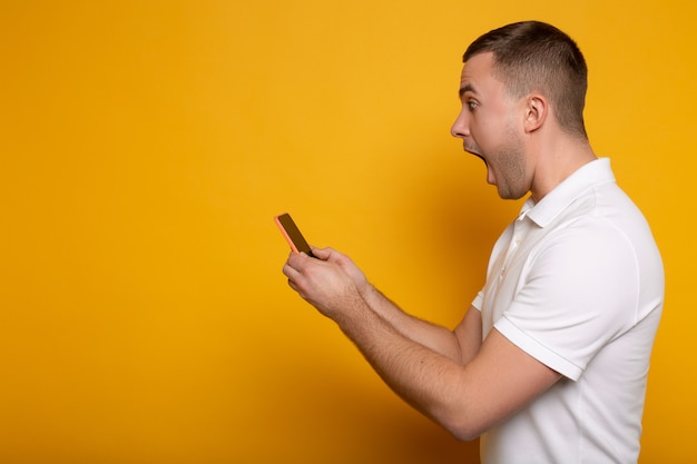 Vista laterale dell'uomo adulto colpito con la bocca aperta facendo uso dello smartphone su giallo