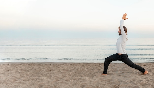 Vista laterale dell'uomo che fa yoga sulla spiaggia con lo spazio della copia