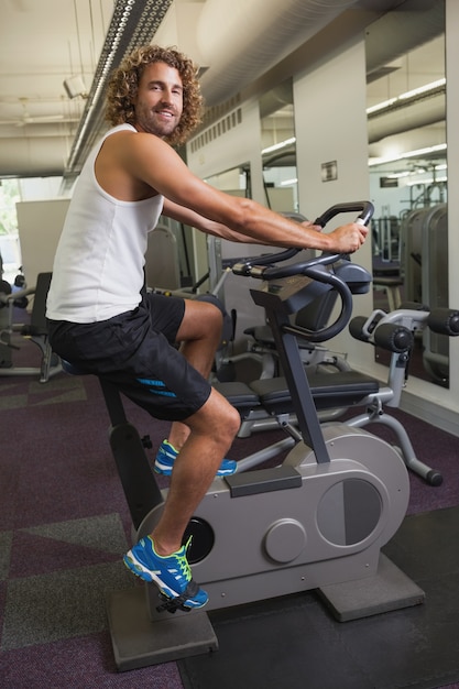 Vista laterale dell&#39;uomo che risolve sulla bici di esercizio alla palestra